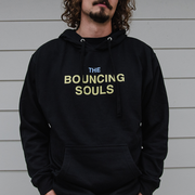 image of a man wearing a black pullover hoodie. front has the text "The Bouncing Souls" in the center chest in yellow and blue ink.