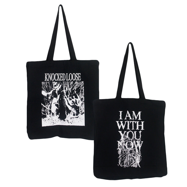 image of the front and back of a black canvas tote bag on a white background. front of the tote bag is on the left and has a full print in white. Knocked loose is written at the top and below that is an image of a persons face with sunglasses on and hands up with white scribbles surrounding it. The back of the tote bag is on the right and has a full print in white that says i am with you now and has white scribbles.