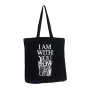 image of the back of a black canvas tote bag on a white background. tote bag has a full print in white that says i am with you now and has white scribbles.
