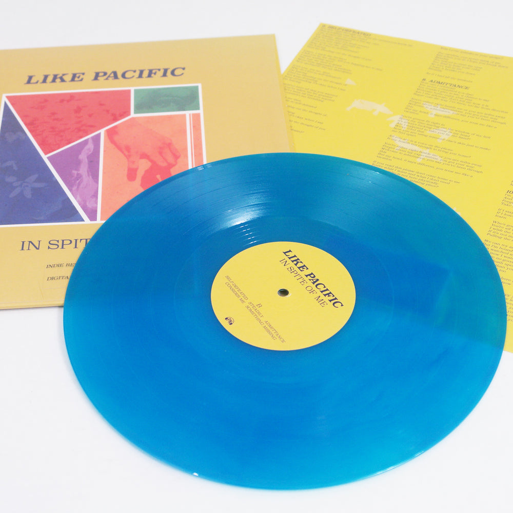 A bright blue Like Pacific vinyl record is displayed with its yellow cover and an inner sleeve featuring lyrics, liner notes, and song titles such as “Sedatives” and “Occupy Your Skin.”.
