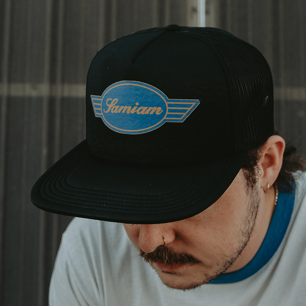 man wearing a black mesh snapback hat. Samiam Logo black Mesh Snapback Hat. Samiam crest logo printed in blue and gold on the front panel of hat. 
