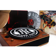 image of record plater with two records in the back and a black slipmat on the records player with a white background.  slipmat is a black circle, with a white circle, the letters P N in the center with white headphones around it. the bottom has arched white text that says pure noise records. the back has a black album cover on left with a grey splatter with a white hand and text on the outer edge. another album cover is on the right and has the word state and a skateboard. 